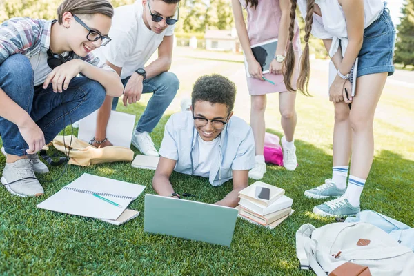 Glückliche multiethnische Teenager lernen mit Büchern und digitalen Geräten im Park — Stockfoto