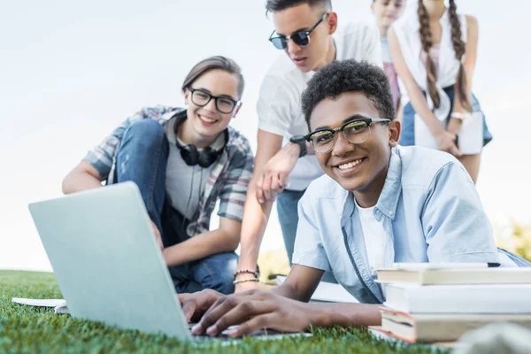 Adolescentes multiétnicos felizes usando laptop e estudando no parque — Fotografia de Stock