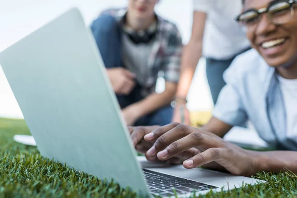 Close-up view of teenagers lying on grass and using laptop — Stock Photo