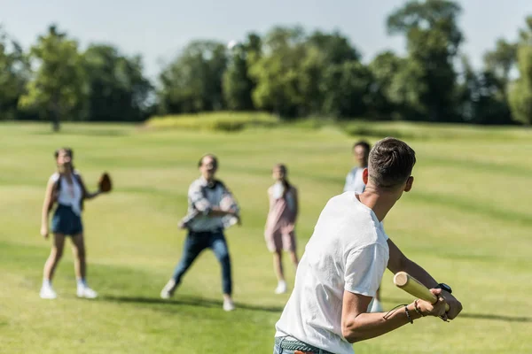 Adolescent garçon tenant chauve-souris et jouer au baseball avec des amis dans le parc — Photo de stock