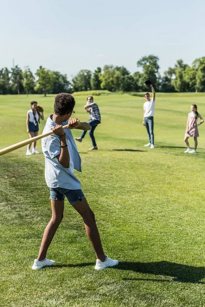 Niño afroamericano jugando béisbol con amigos adolescentes en el parque - foto de stock