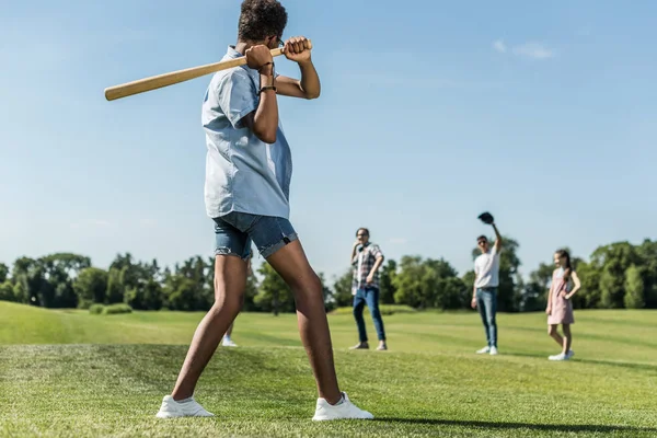 Afroamericano adolescente sosteniendo béisbol bat y jugando con amigos en parque - foto de stock