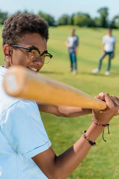 Foco seletivo de sorrir adolescente afro-americano jogando beisebol com amigos no parque — Fotografia de Stock
