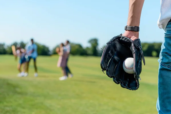 Cropped shot of teenager in baseball glove holding ball while playing with friends in park — Stock Photo