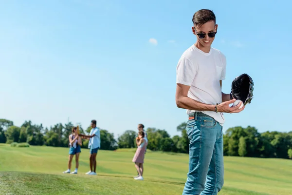 Smiling teenage boy playing baseball with friends in park — Stock Photo