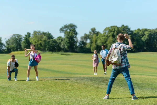 Happy teenage friends playing baseball on green meadow in park — Stock Photo