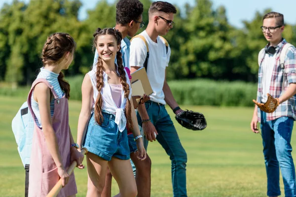 Amici adolescenti felici con libri e zaini che giocano a baseball nel parco — Foto stock