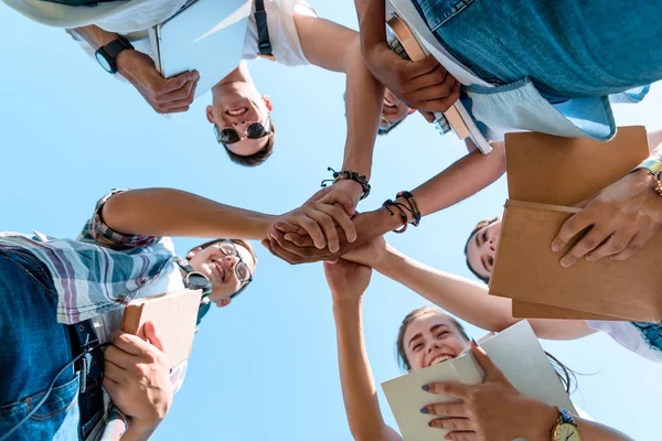 Bottom view of smiling multiethnic teenage classmates stacking hands in park — Stock Photo