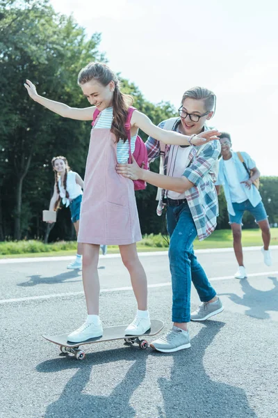 Feliz adolescente enseñanza chica montar monopatín en parque - foto de stock