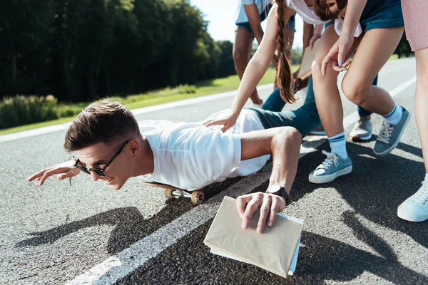 Cropped shot of teenagers having fun while friend lying on skateboard — Stock Photo