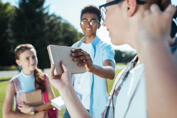 Plan recadré de l'adolescent donnant livre à un ami souriant dans le parc — Photo de stock