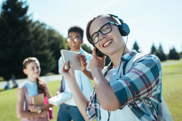 Sonriente adolescente en auriculares dando libro a amigo en parque - foto de stock