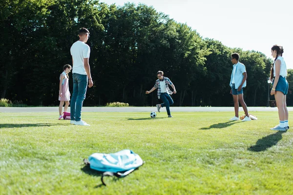 Multiethnic teenage classmates playing with soccer ball in park — Stock Photo
