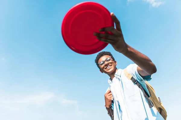 Tiefansicht glücklicher afrikanisch-amerikanischer Teenager mit fliegender Scheibe gegen blauen Himmel — Stockfoto