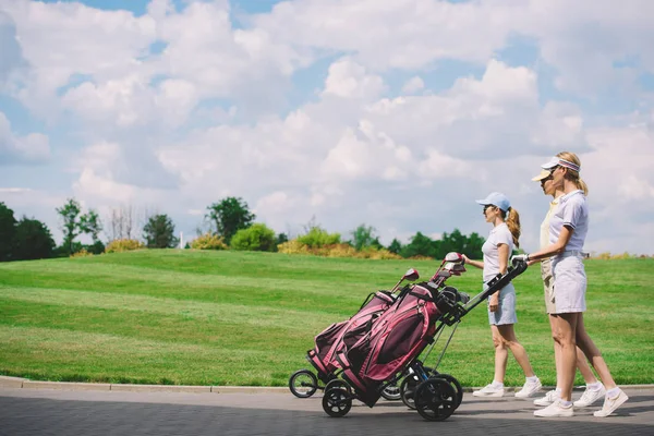 Vista laterale di golfisti di sesso femminile con attrezzature da golf a piedi al campo da golf — Foto stock