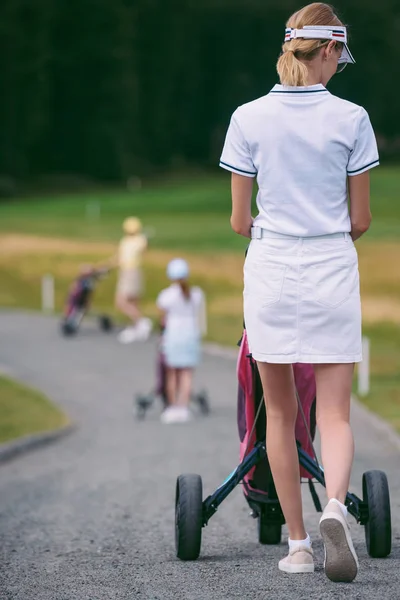 Foco seletivo de jogador de golfe feminino em boné e pólo branco com equipamento de golfe no campo de golfe — Fotografia de Stock