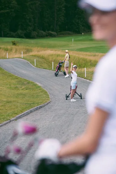 Messa a fuoco selettiva della donna in occhiali da sole con attrezzi da golf saluto amico al campo da golf — Foto stock