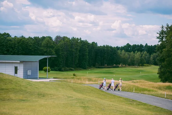 Golfisti di sesso femminile con attrezzi da golf a piedi al campo da golf nella giornata estiva — Foto stock