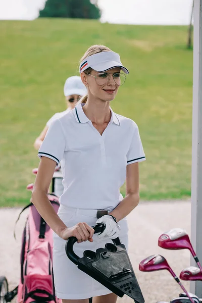 Retrato de mujer sonriente en gorra, guante de golf y polo en campo de golf - foto de stock