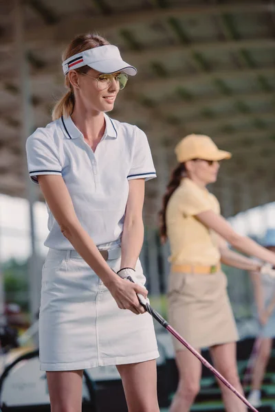 Избирательный фокус улыбающейся женщины, играющей в гольф с другом на поле для гольфа — стоковое фото