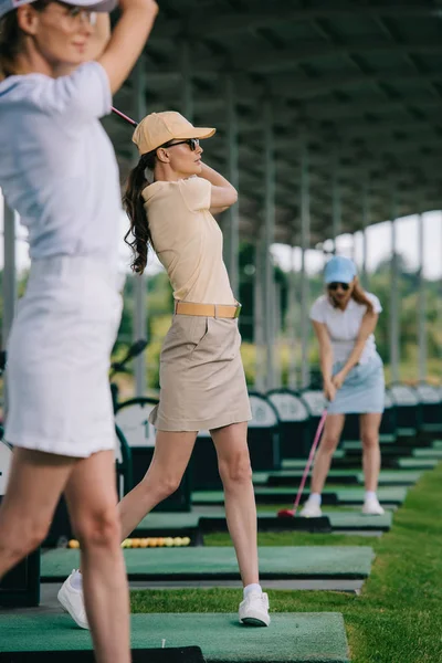 Селективное внимание женщин в шапках, играющих в гольф на поле для гольфа — стоковое фото