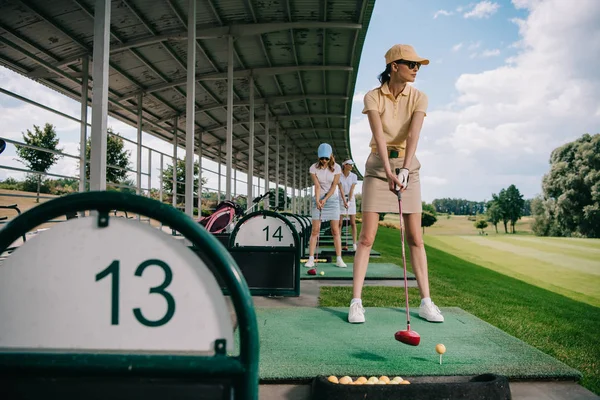 Mujeres en gorras con palos de golf jugando al golf en el campo de golf - foto de stock