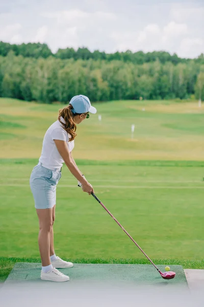 Вид збоку жінки в поло і шапка грає в гольф на полі для гольфу — стокове фото