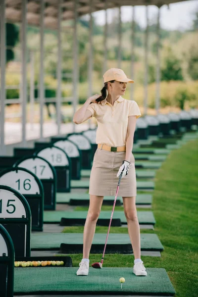 Femme en casquette jaune et polo jouant au golf sur le terrain de golf — Photo de stock