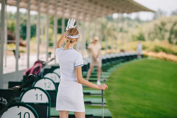 Back view of female golfer with golf club greeting friend at golf course — Stock Photo