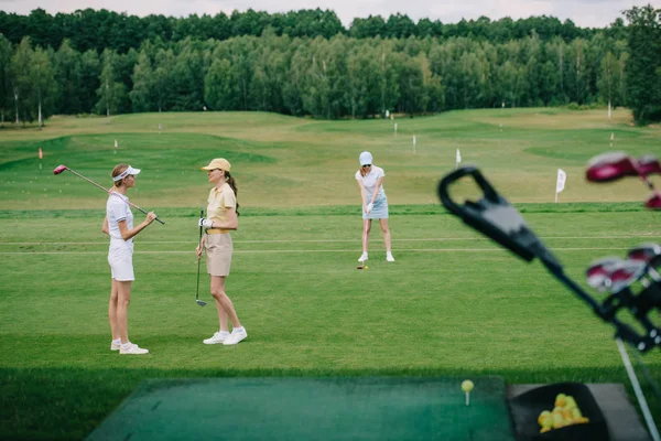 Selective focus of women in caps with golf equipment at golf course — Stock Photo