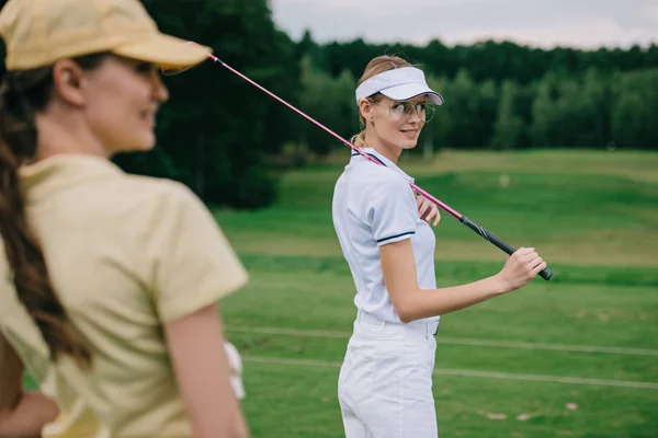 Foco seletivo de mulheres sorridentes em bonés com equipamento de golfe no campo de golfe — Fotografia de Stock