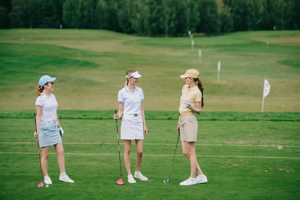 Mulheres em bonés com equipamento de golfe conversando no campo de golfe — Fotografia de Stock