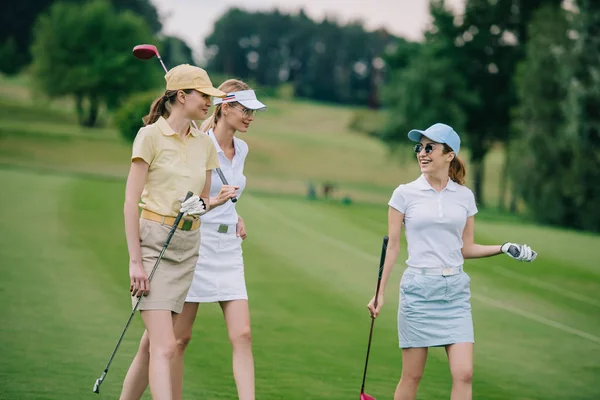 Женщины в шапках с оборудованием для гольфа беседуют на поле для гольфа — стоковое фото