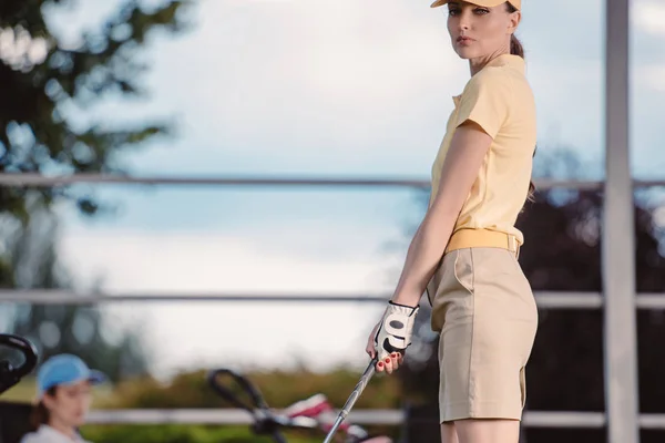 Messa a fuoco selettiva del giocatore di golf femminile che gioca a golf mentre l'amico riposa dietro al campo da golf — Foto stock