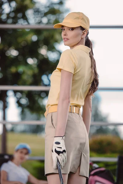 Foyer sélectif du joueur de golf féminin avec club de golf et ami se reposant derrière au terrain de golf — Photo de stock