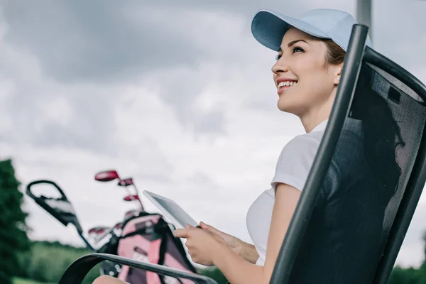 Vue à angle bas du joueur de golf féminin gai en casquette avec tablette dans les mains — Photo de stock