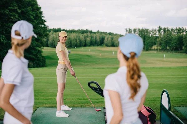 Foco seletivo de sorrir jogador de golfe feminino olhando para os amigos no campo de golfe — Fotografia de Stock