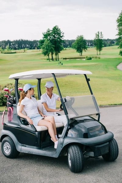 Female golfers in caps looking at each other in golf cart at golf course — Stock Photo