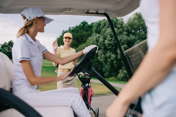 Sonriente jugadora de golf saludando amiga en carrito de golf en campo de golf - foto de stock