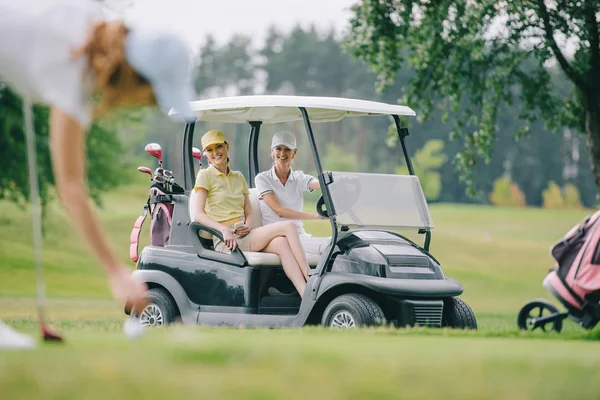 Focus selettivo della donna che gioca a golf mentre gli amici cavalcano golf cart al campo da golf — Foto stock