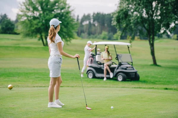 Foyer sélectif de la femme avec club de golf à la recherche d'amis se reposant à la voiturette de golf sur la pelouse verte — Photo de stock