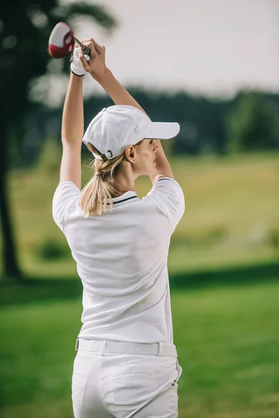Back view of female golf player in cap with golf club in hands at golf course — Stock Photo