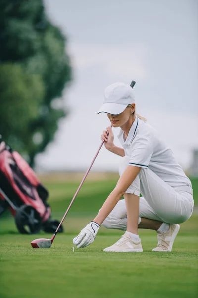 Joueuse de golf en bonnet et gant de golf mettant la balle sur la pelouse verte au terrain de golf — Photo de stock