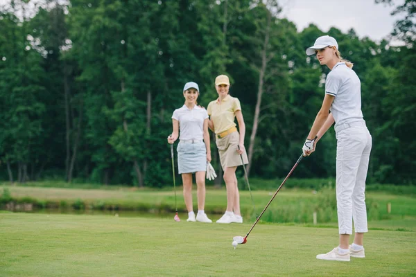 Enfoque selectivo de la mujer en la gorra jugando al golf, mientras que los amigos de pie cerca en el campo de golf - foto de stock