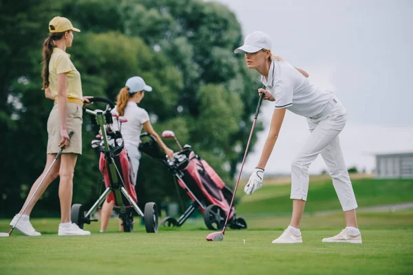 Enfoque selectivo de la mujer enfocada en la gorra jugando al golf con amigos cerca en el campo de golf - foto de stock