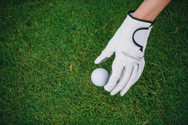 Vista parcial de la mujer en el guante de golf poniendo pelota en el césped verde en el campo de golf - foto de stock