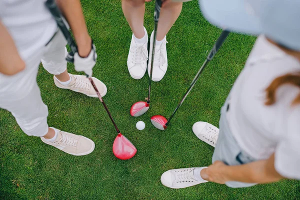 Overhead view of female golf players with golf clubs standing on green lawn with golf ball in middle — Stock Photo