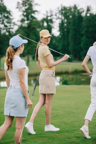 Vista parcial de mulheres em bonés com equipamento de golfe andando no gramado verde no campo de golfe — Fotografia de Stock