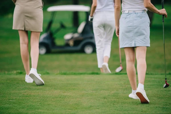 Обрезанный снимок женщин с клюшками для гольфа, идущих по зеленой лужайке на поле для гольфа — стоковое фото