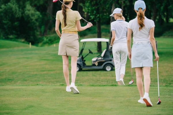 Вид сзади на женщин с клюшками для гольфа, прогуливающихся по зеленой лавке на поле для гольфа — стоковое фото